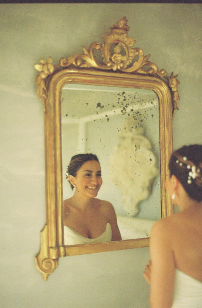 Bride looks at her reflection in historic, ornate mirror as she gets ready for her ​Sicily wedding photographer to capture the day. 