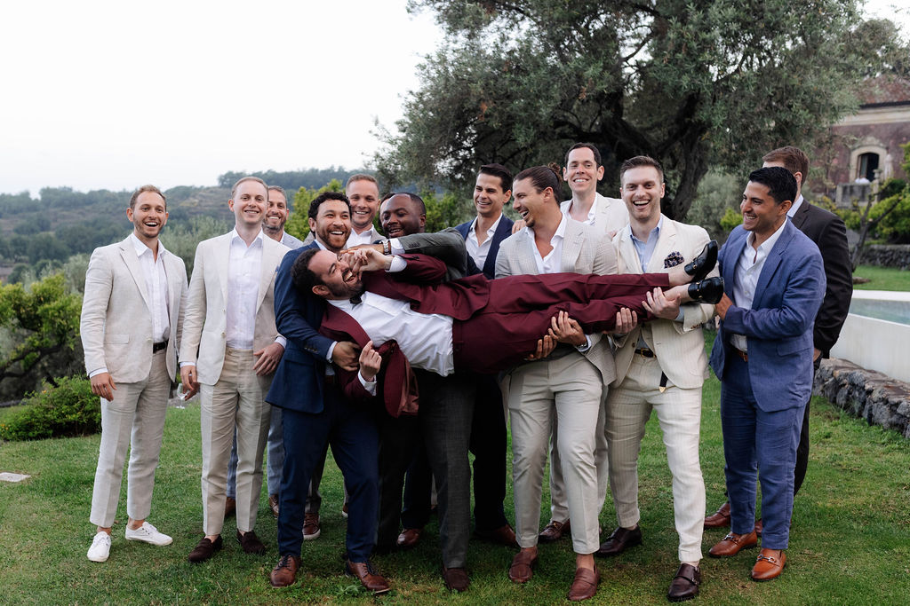 Destination wedding in Sicily captures groom being held by his friends during outdoor portraits. 